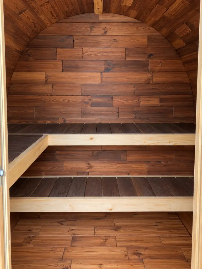 Blick durch den Eingang der Ovoid Sauna auf Holzverkleidung und zweistufige Saunabänke